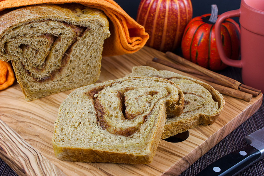 Pumpkin Cinnamon Swirl Bread loaf sliced on a wooden cutting board.