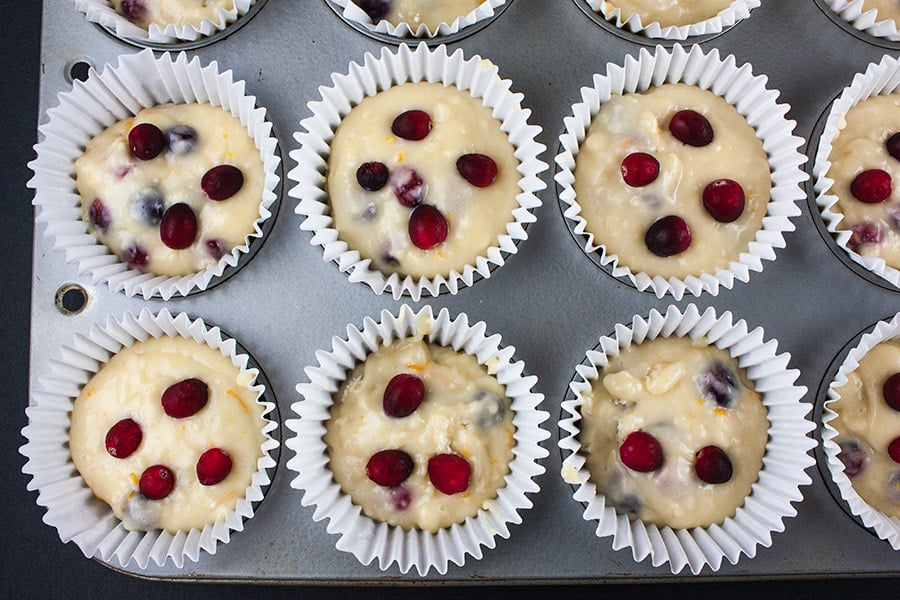 Cranberry orange muffin batter in large white liners in muffin tin.
