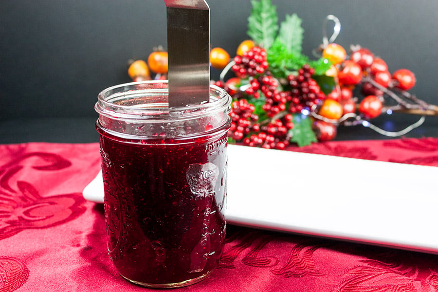 cranberry sauce in a glass jar with a thin metal spatula running along the inside of the jar