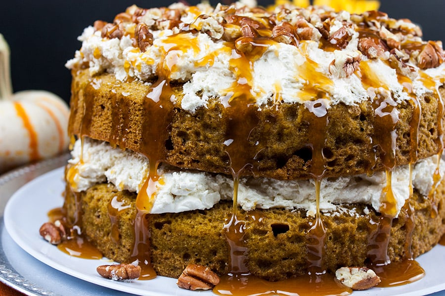 pumpkin cake with whipped cream cheese filling topped with pecans and caramel drizzle on white cake plate