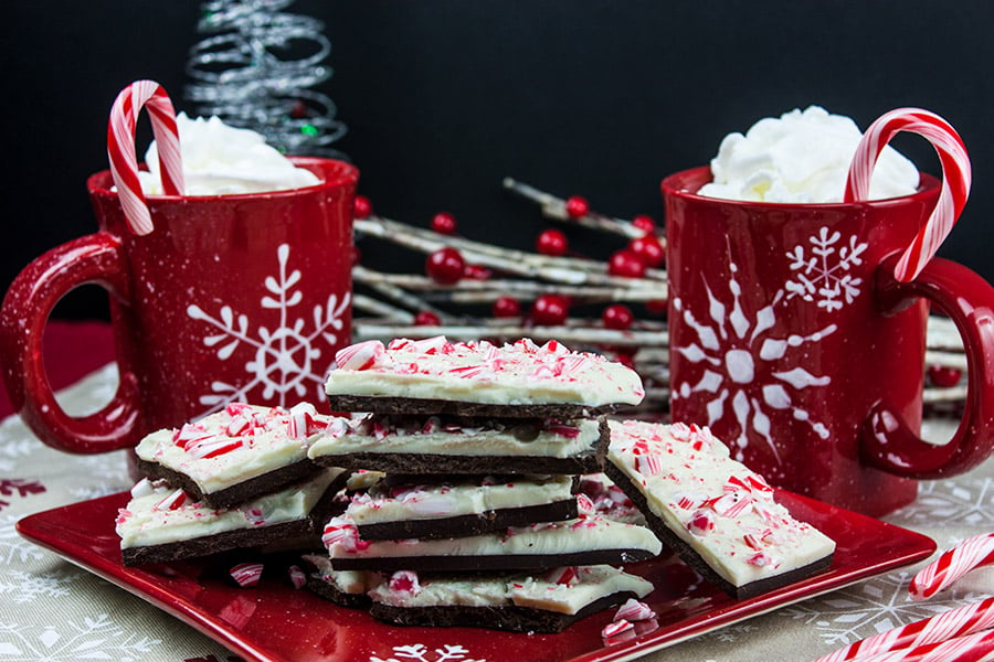 Dark chocolate peppermint bark stacked on a plate with Christmas coffee mugs behind it.