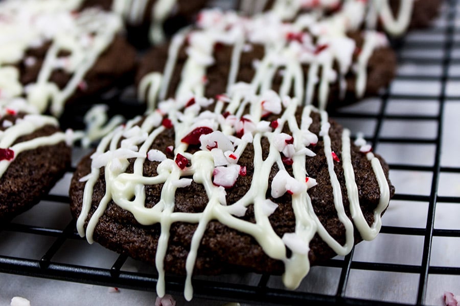 Chocolate Peppermint Cookies drizzled with white chocolate and topped with crushed candy canes on a wire rack.