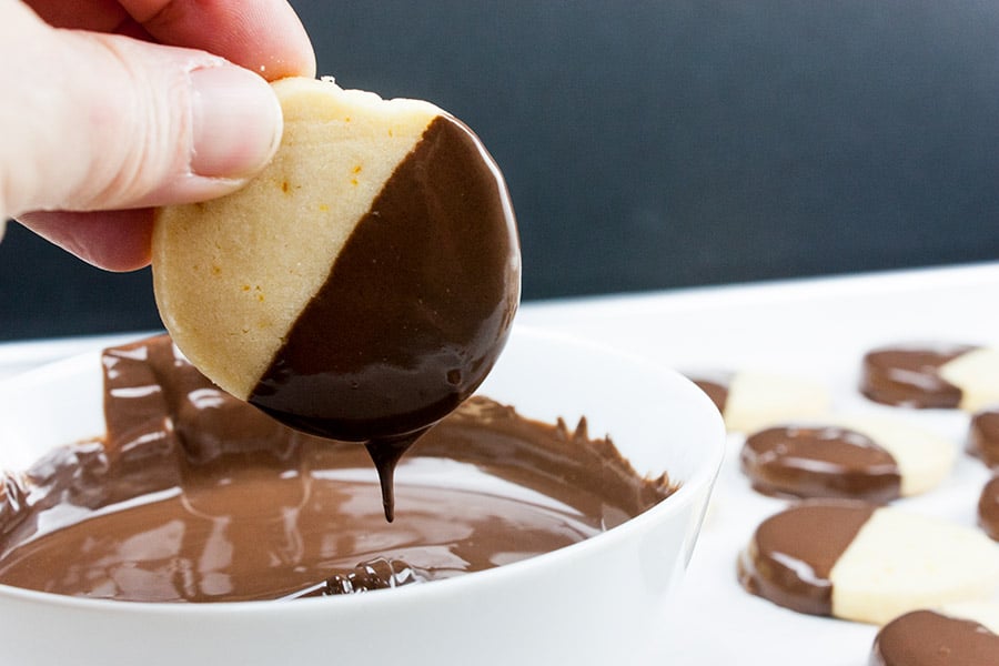Baked orange shortbread cookie dipped into melted chocolate dripping off the excess.