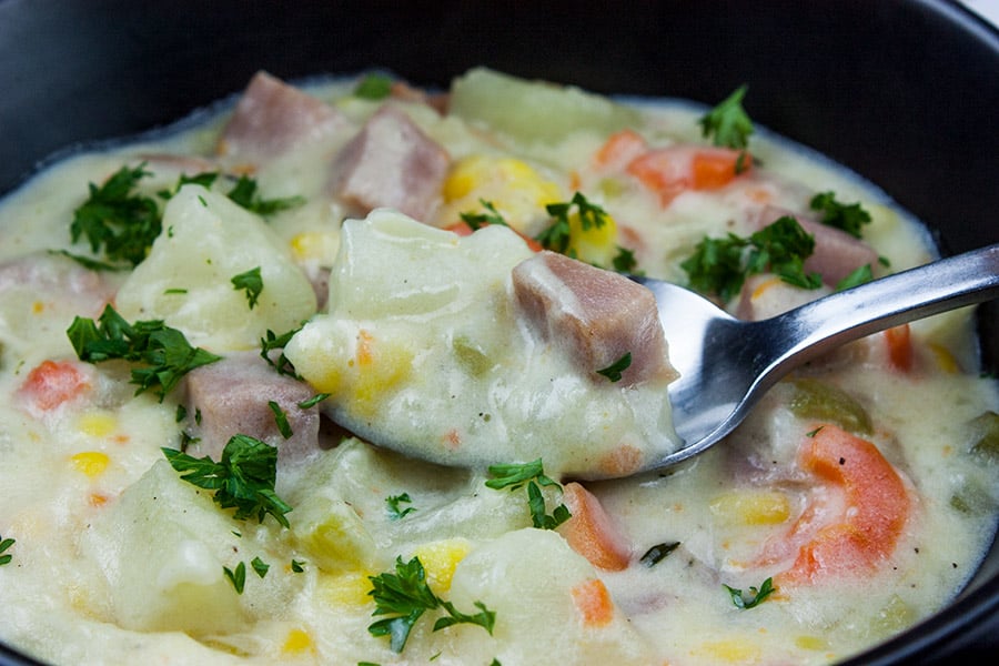 Easy ham and potato soup served in dark bowl garnished with chopped parsley.