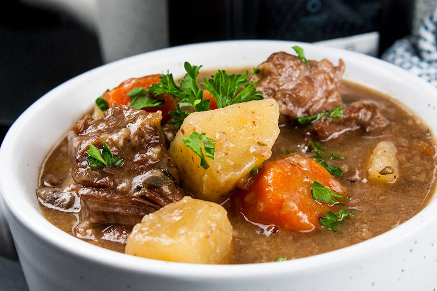 Slow Cooker Beef Stew in a white bowl garnished with chopped parsley.
