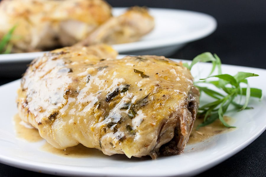 Roasted chicken leg quarter with dijon cream sauce on a plate garnished with fresh tarragon.