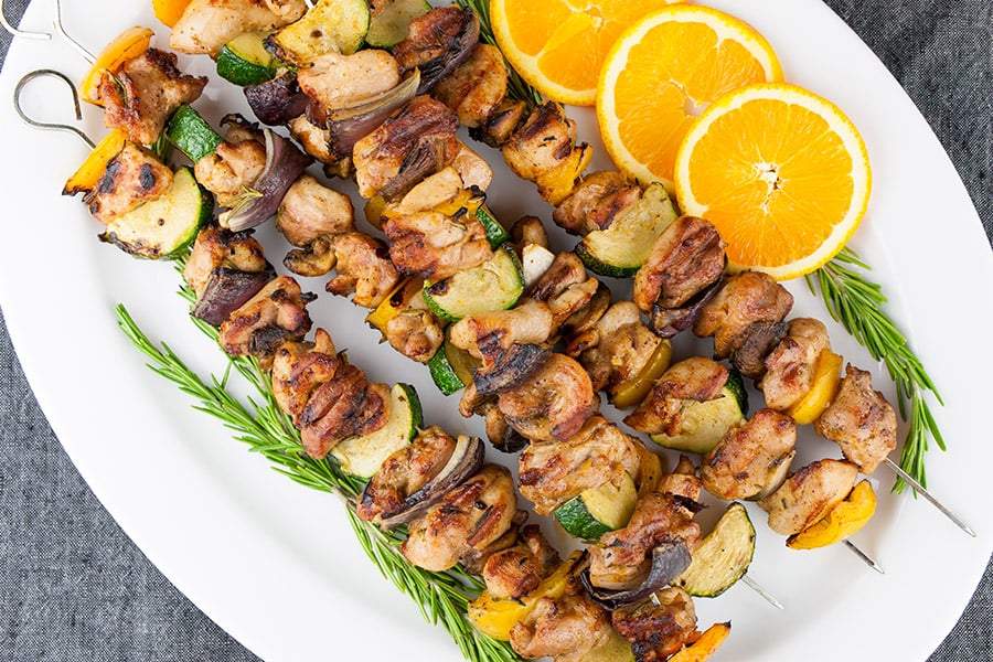 Orange Rosemary Chicken Kebabs on white platter garnished with orange slices and fresh rosemary