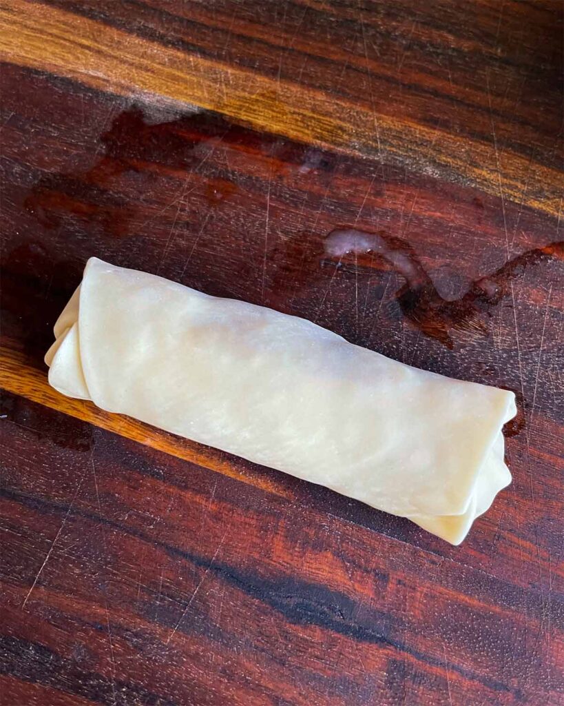 An uncooked redneck egg roll on a wooden cutting board.
