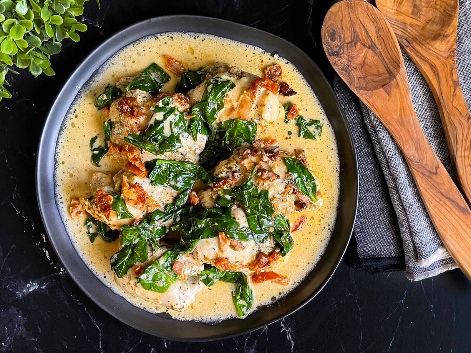 Tuscan chicken in a dark bowl on a dark surface.