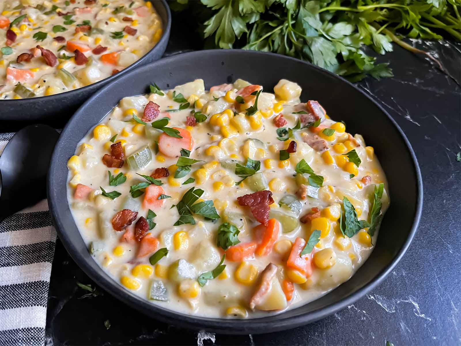 Creamy potato corn chowder in a dark bowl on a dark surface.