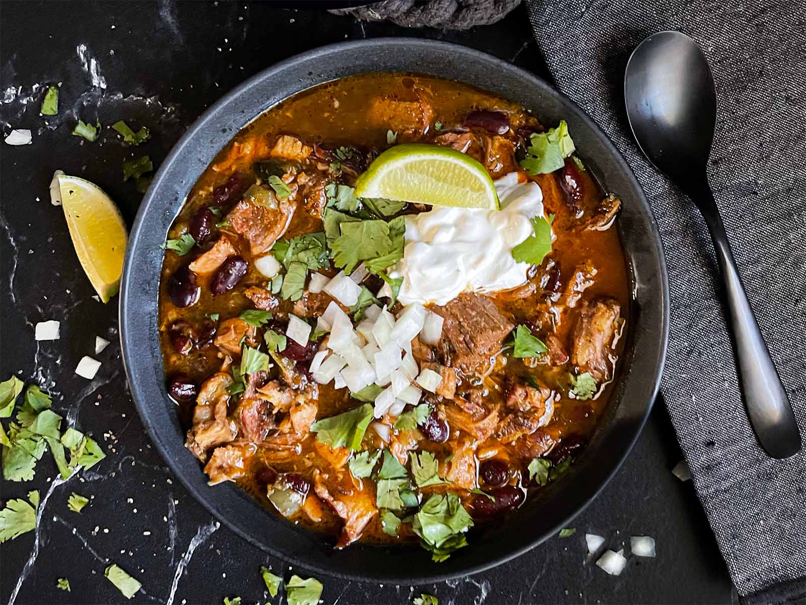 Smoked pork chili in a dark bowl garnished with diced onion and cilantro.