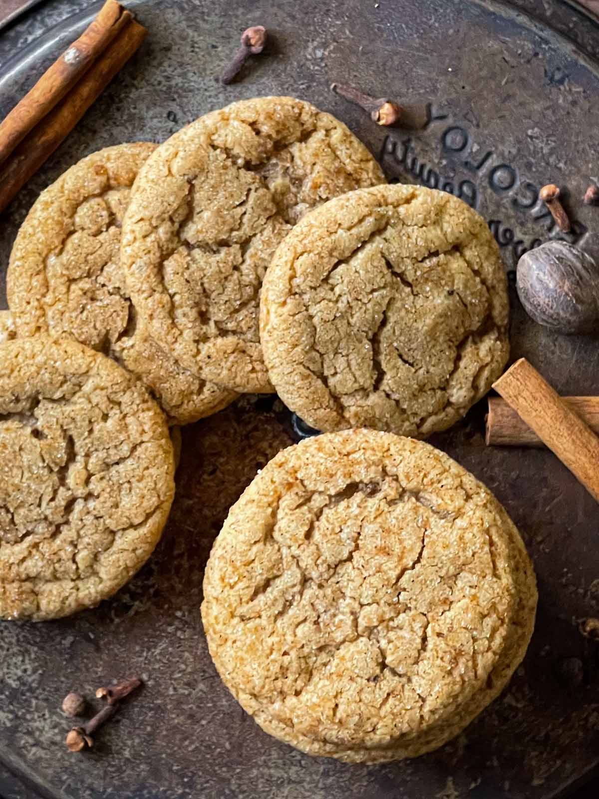 Chai sugar cookies on a dark surface with cinnamon sticks, nutmeg, and cloves.