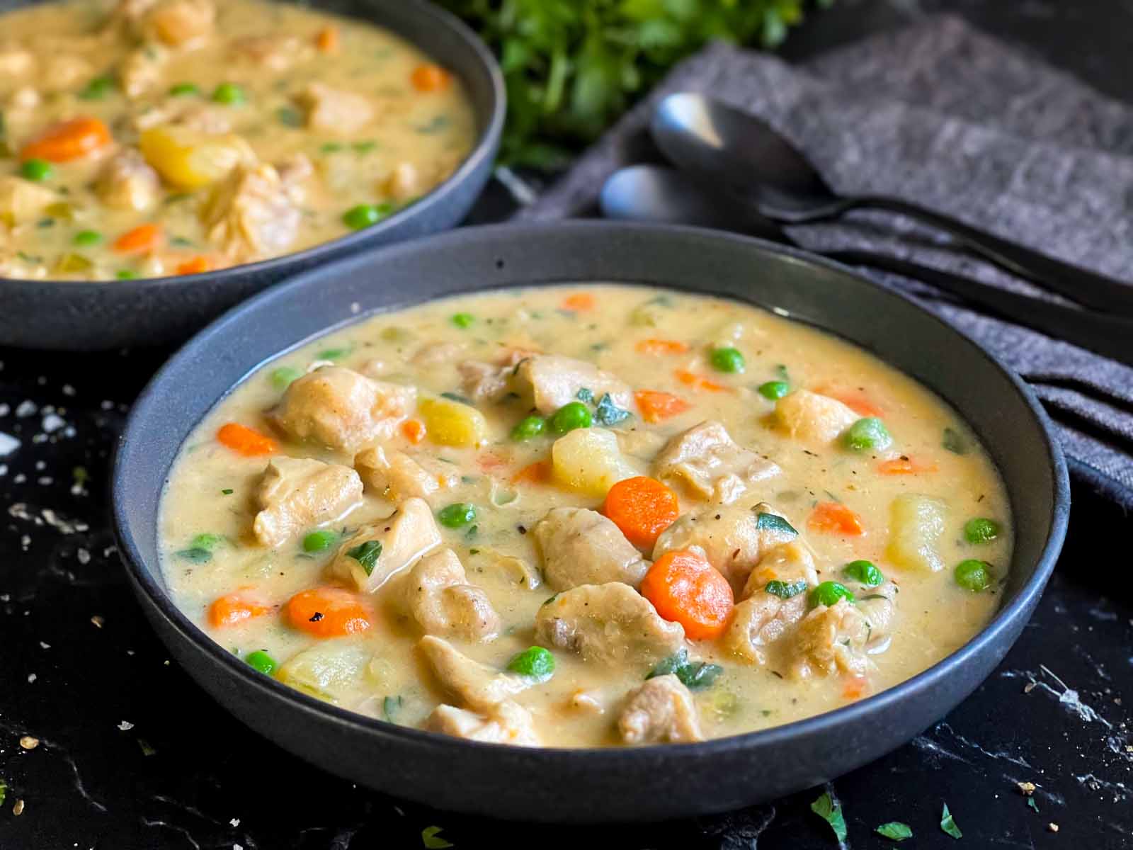 Creamy chicken stew in a dark bowl on a dark surface.