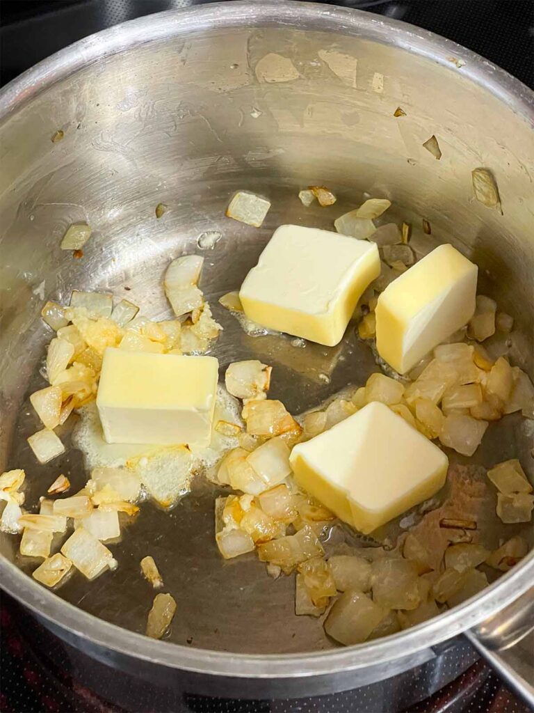 Adding butter to onions and garlic cooking in a pot.