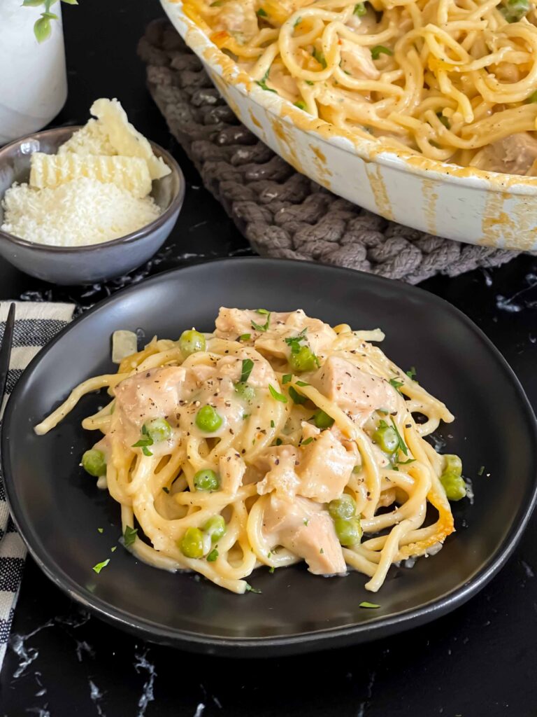 Chicken tetrazzini in a white baking dish with a serving on a dark plate.