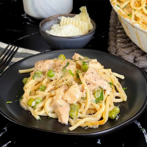 Chicken tetrazzini in a white baking dish with a serving on a dark plate.