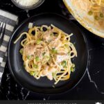 Chicken tetrazzini in a white baking dish with a serving on a dark plate.