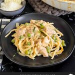 Chicken tetrazzini in a white baking dish with a serving on a dark plate.