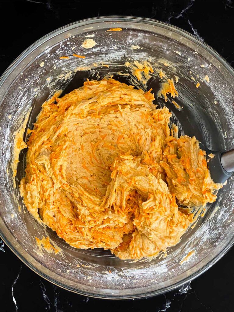 Carrot coffee cake batter mixed in a glass mixing bowl on a dark surface.