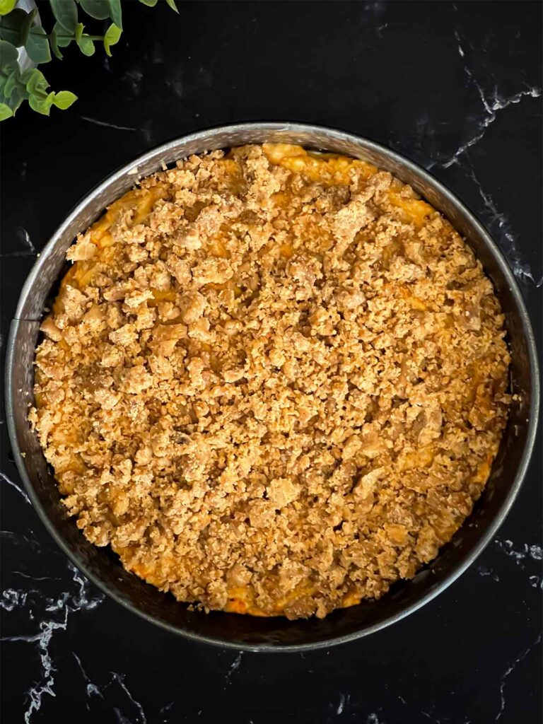 Carrot coffee cake batter and streusel in a prepared springform pan on a dark surface.