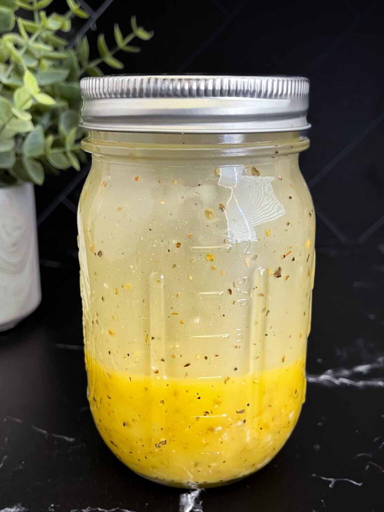 Marinated cauliflower salad dressing mixed in a mason jar on a dark surface.