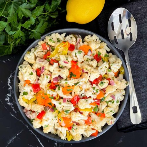 Marinated cauliflower salad in a dark bowl on a dark surface.