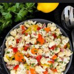 Marinated cauliflower salad in a dark bowl on a dark surface.