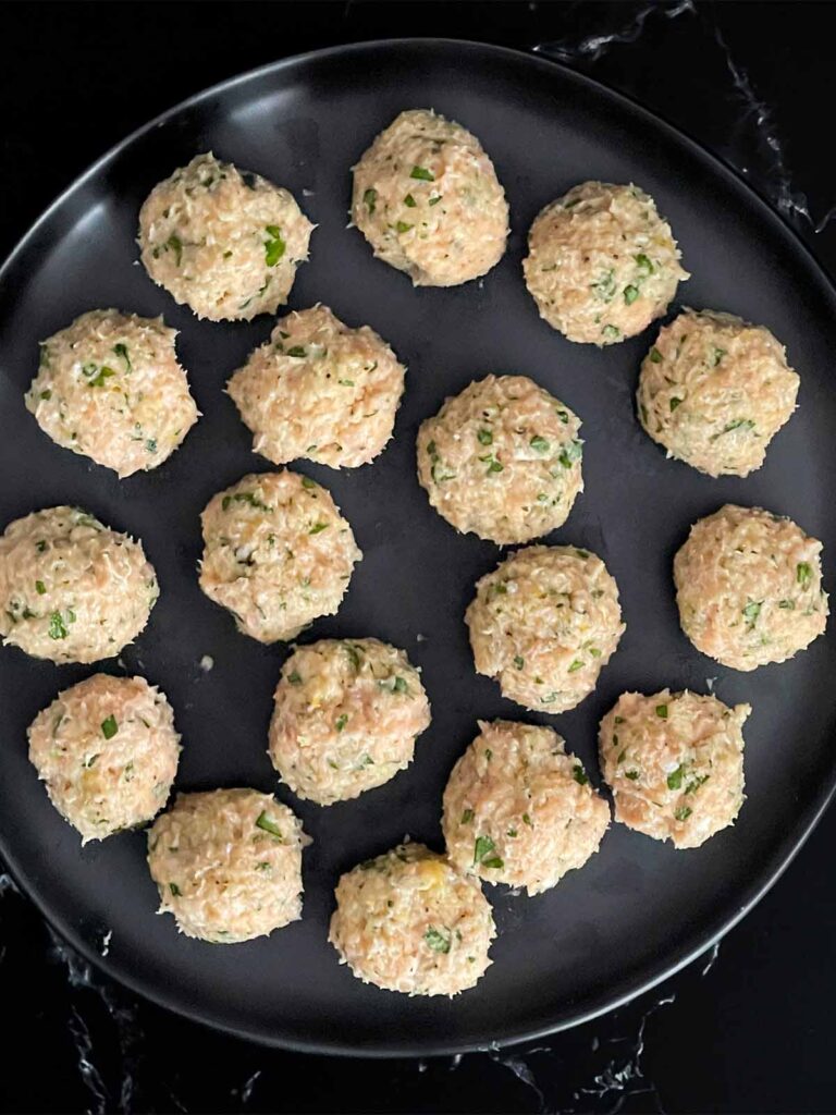 Chicken Piccata Meatballs on a dark plate, uncooked.