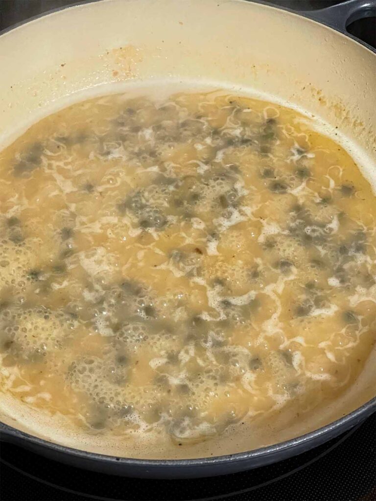 A piccata sauce cooking in a skillet.