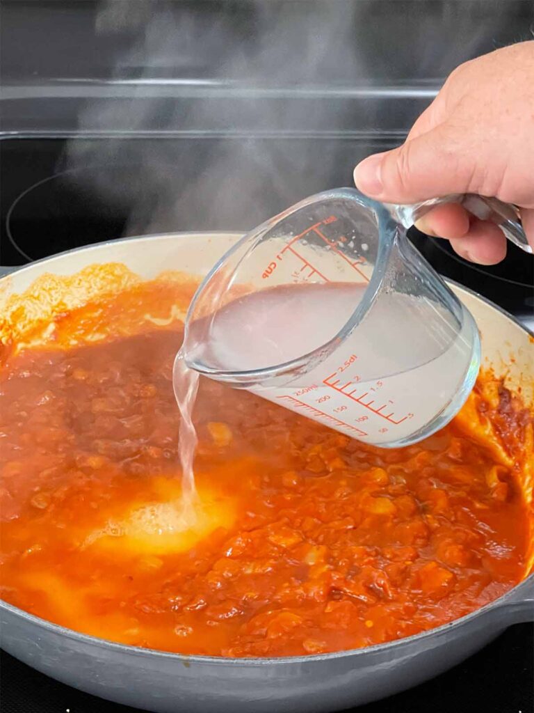 Adding pasta water to Vodka sauce cooking in a skillet.