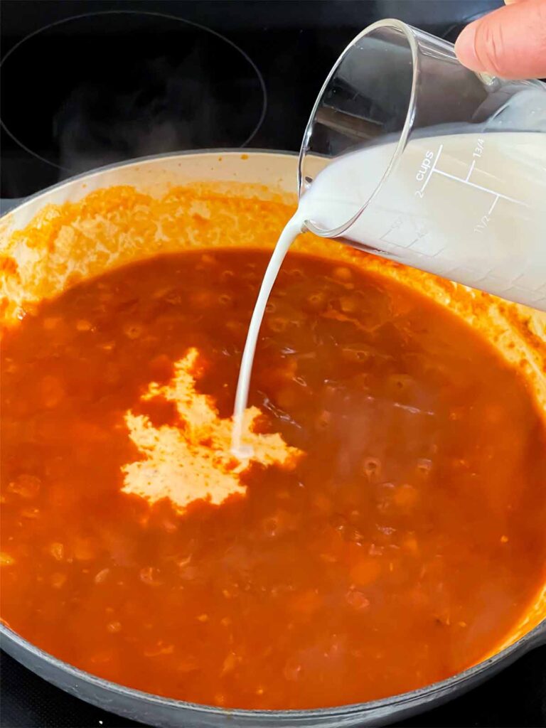 Adding cream to Vodka sauce cooking in a skillet.