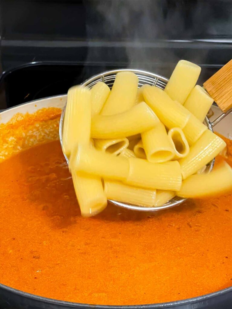 Adding pasta to Vodka sauce cooking in a skillet.