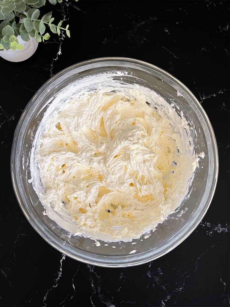 Whipped topping mixed into the cheesecake mixture in a glass mixing bowl on a dark surface.
