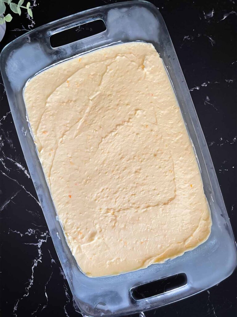 Coconut cream pudding mixture spread over the cheesecake layer in a glass baking pan.