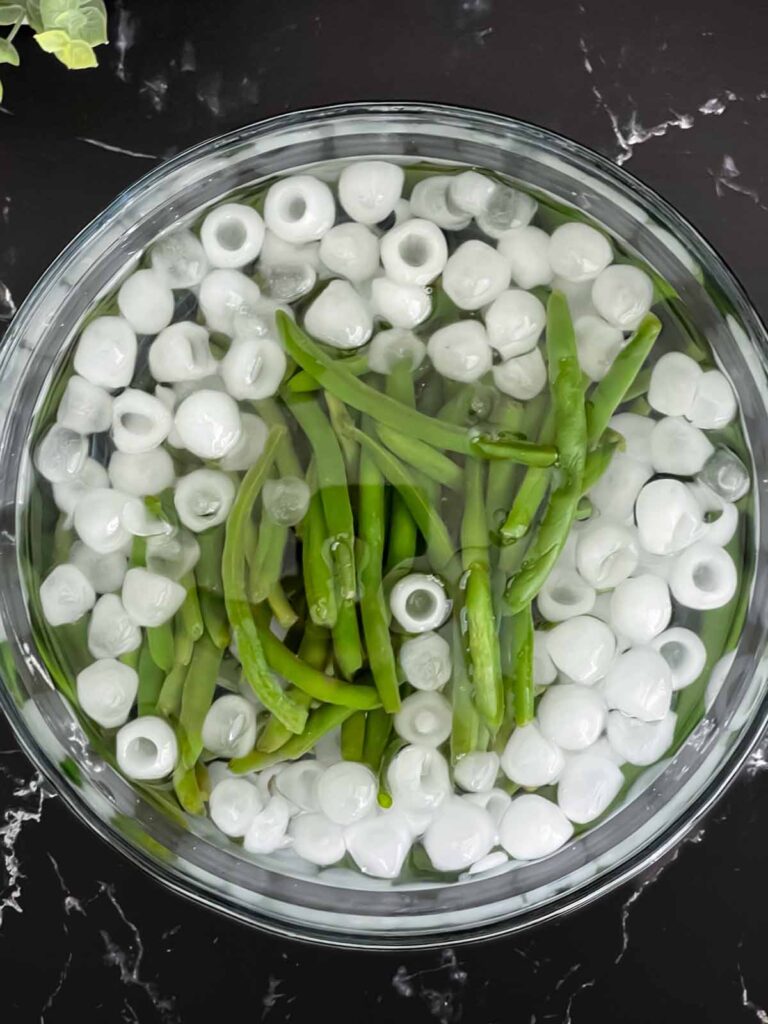 Fresh green beans in a glass boil of ice water.