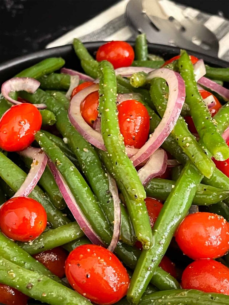 Italian green bean salad in a dark bowl on a dark surface.