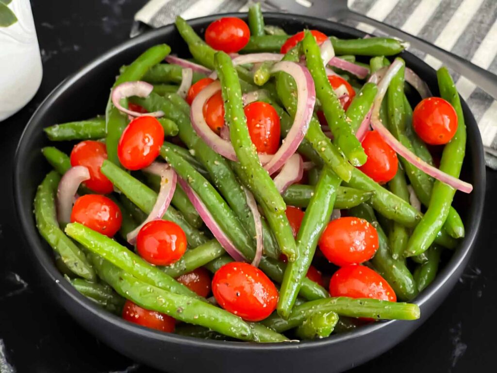 Italian green bean salad in a dark bowl on a dark surface.