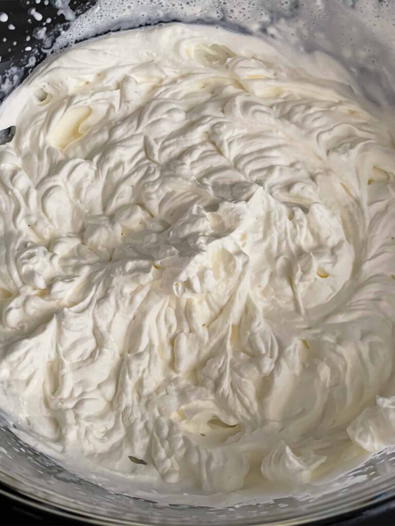 Whipped heavy cream in a glass mixing bowl.