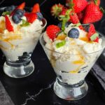 Ricotta mousse in a stemless martini glass garnished with strawberries, blueberries, basil, and honey.