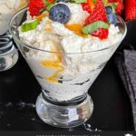 Ricotta mousse in a stemless martini glass garnished with strawberries, blueberries, basil, and honey.