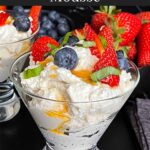 Ricotta mousse in a stemless martini glass garnished with strawberries, blueberries, basil, and honey.