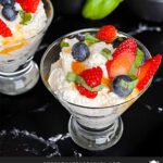 Ricotta mousse in a stemless martini glass garnished with strawberries, blueberries, basil, and honey.