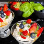 Ricotta mousse in a stemless martini glass garnished with strawberries, blueberries, basil, and honey.