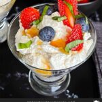 Ricotta mousse in a stemless martini glass garnished with strawberries, blueberries, basil, and honey.