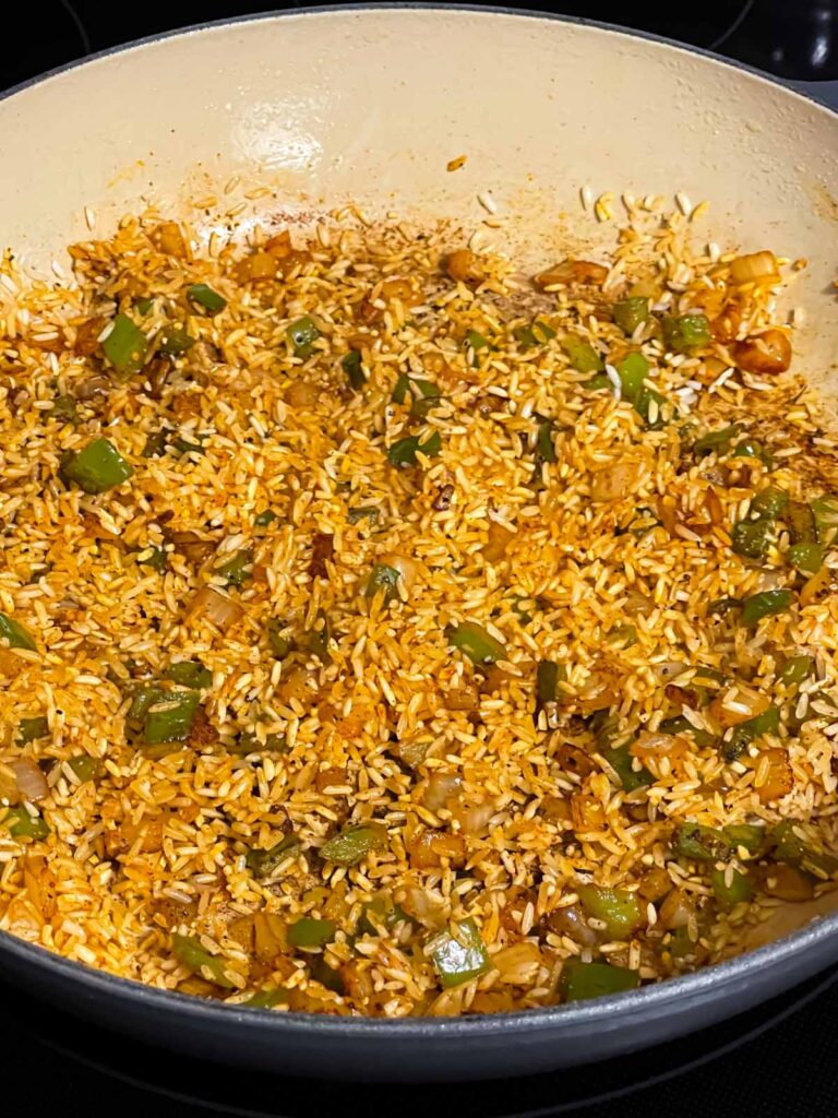 White rice, onions, green peppers, and seasonings tossed in a skillet for Spanish pork chops and rice recipe.