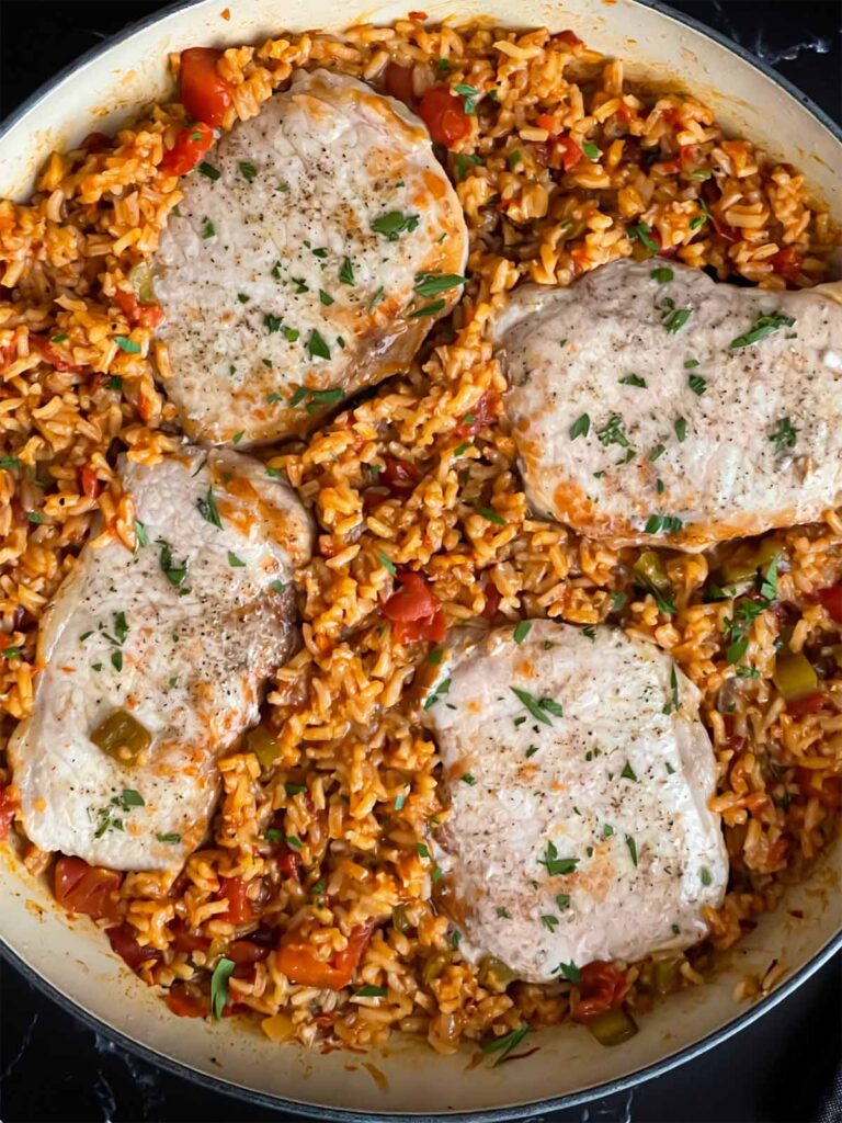 Spanish pork chops and rice garnished with chopped parsley in a light colored skillet.