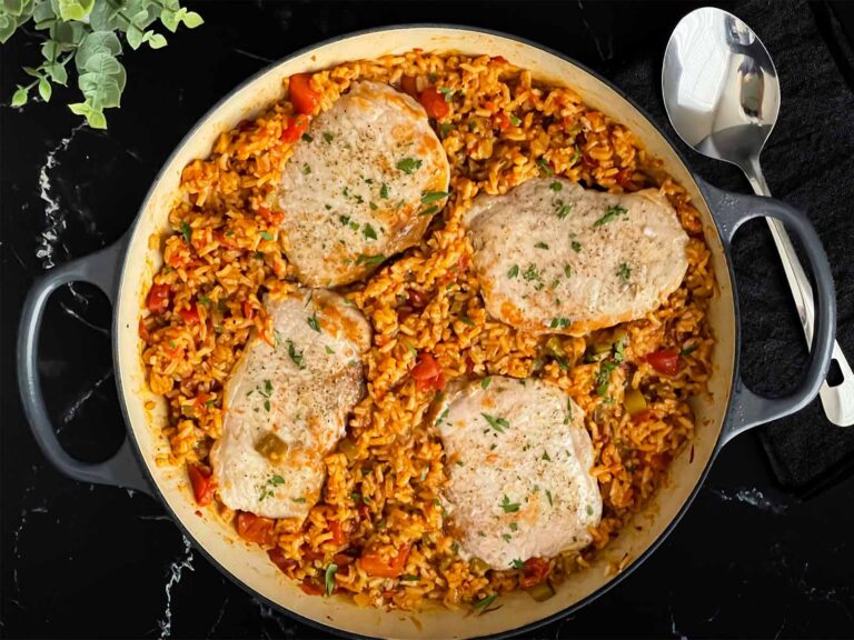 Spanish pork chops and rice garnished with chopped parsley in a light colored skillet.