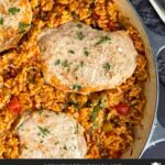 Spanish pork chops and rice garnished with chopped parsley in a light colored skillet.