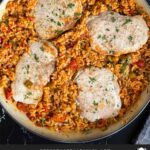 Spanish pork chops and rice garnished with chopped parsley in a light colored skillet.