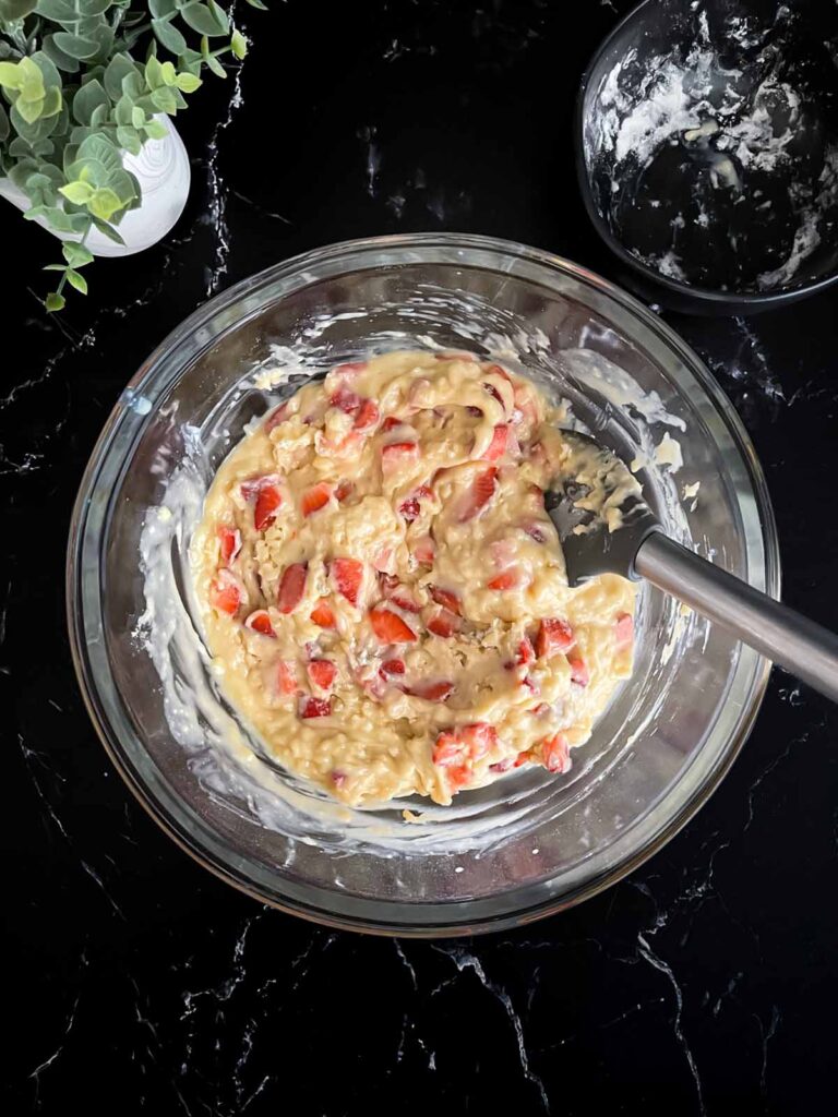 Strawberry muffin batter in a glass mixing bowl on a dark surface.